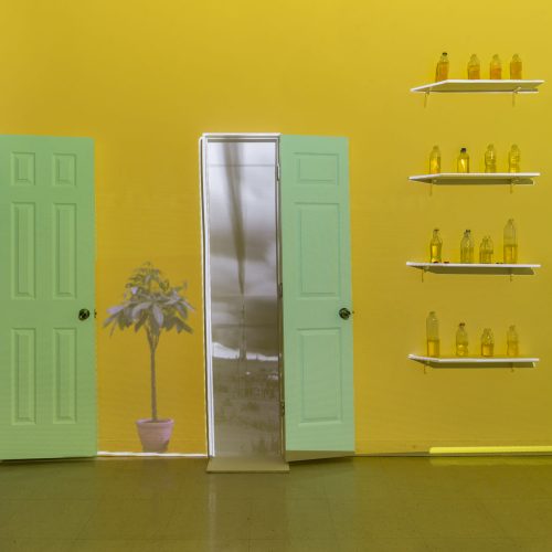 Video still of 3D modeled space, with two green doors and eight shelves with plastic water bottles on them, against a yellow wall.