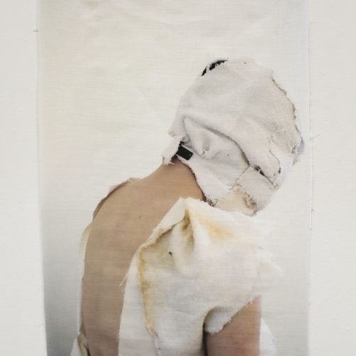 Image of a woman whose face is wrapped in cloth printed on a piece of fabric and hung on the wall.