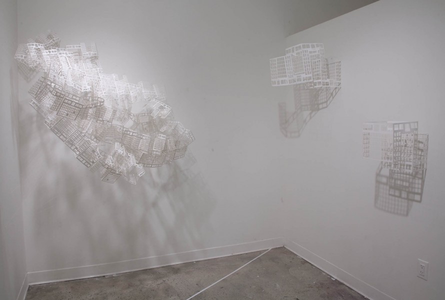 Installation view of Paper thread. On the left side is a large structure like a mesh made out of white material, and on the right are two structures made out of the same material, looking like a mesh. All three structures are mounted on a wall.