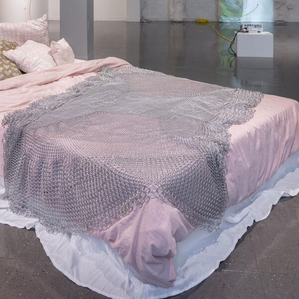 Chainmail blanket on bed with pink and white sheets.