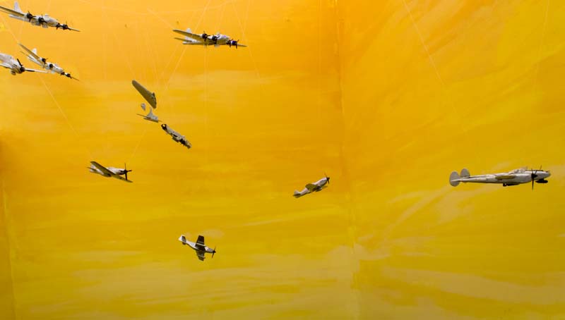 Miniature military planes hung with invisible wire on a yellow background.