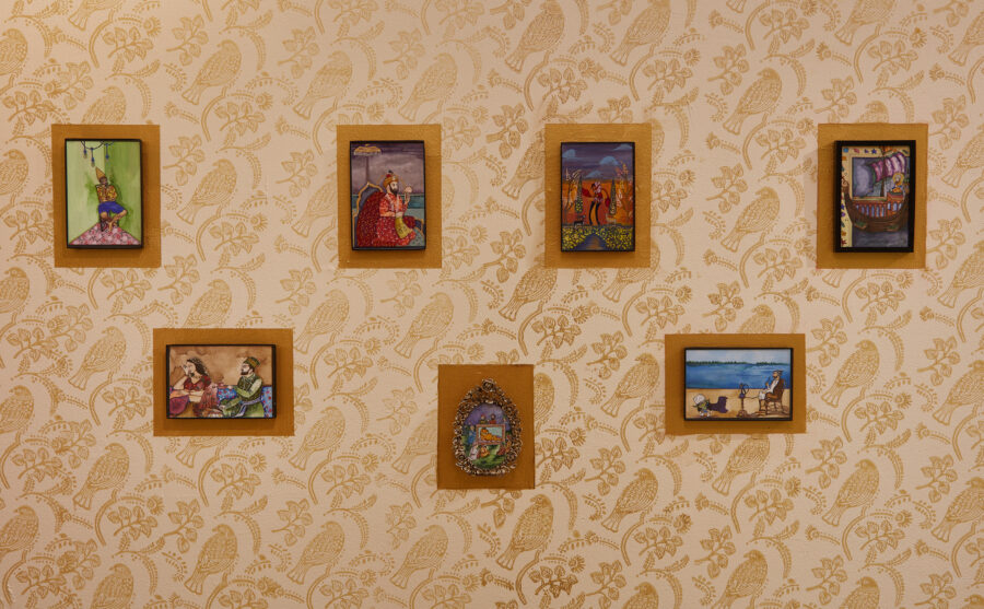 An installation shot of seven framed miniatures out of fourteen hung on a patterned wall with house paint.