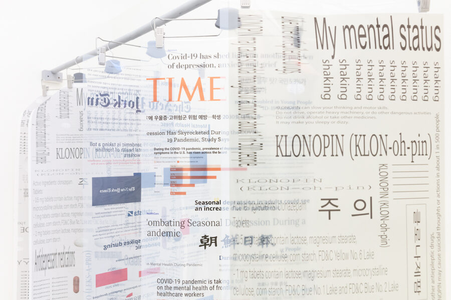 Various typography in English and Korean printed on sheets of vellum suspended by metal pants hangers on a white wooden rod.