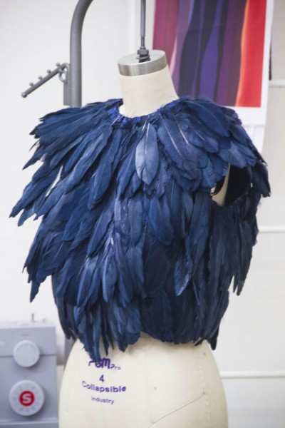 A student art work being constructed of blue feathers on a dress form in the Wearable Art class