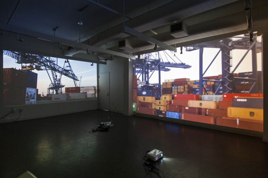 Installation view of two image projectors projecting images of shipping containers and craines.