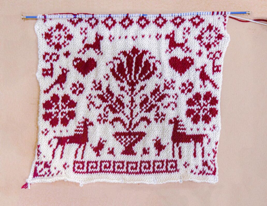A knitting piece in dark red and white with animals, hearts and floral motives. 