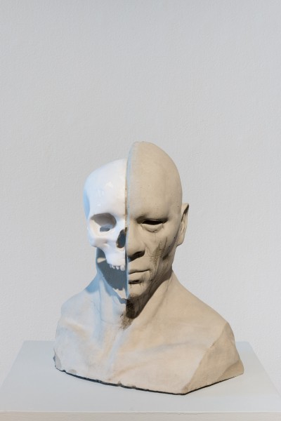 A white sculpture of a head with a normal half of the face and a skull part of the face.