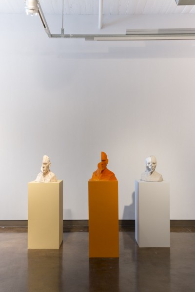 Installation view of sculptures with half of the head in beige color, orange, and white.