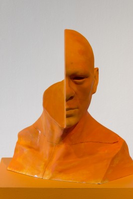 An orange bust sculpture of a man with his half head cut.