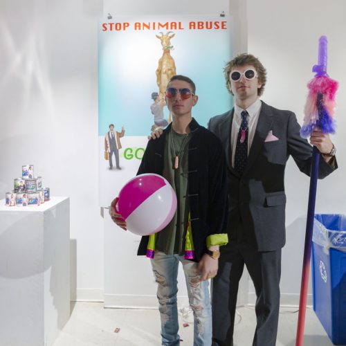 Portrait of two young men one with his hand on the other's shoulder, standing among their installation.