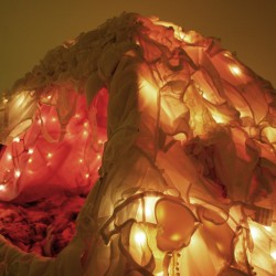 A tent made of bras and fairy lights inside, installed on a dark room