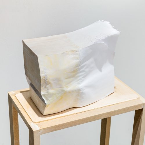 A sculpture by Hanjun Zhang. A rectangular object with muted hues placed on a wooden table..