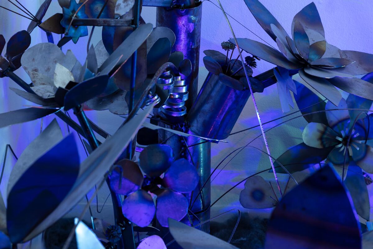 Installation view of steel flowers with a purple light projection.