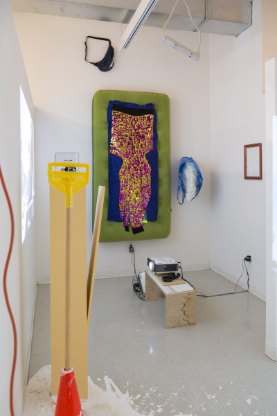 Installation view of sparkle fabric on green matters hanging on the wall, orange cone, and miscellaneous objects.