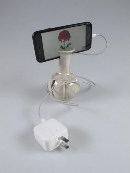 Ceramic vase with Iphone inserted into it showing a virtual flower growing on screen with a phone charger plugged in.