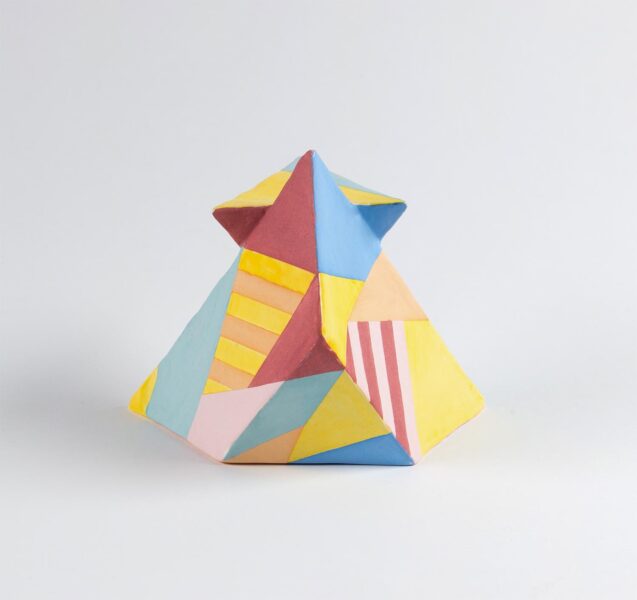 A ceramic sculpture made of sharp geometric shapes. The sculpture is covered in different geometric forms and colors of pink, blue, orange and yellow.