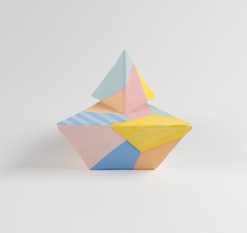 A ceramic sculpture made of sharp geometric shapes. The sculpture is covered in different geometric forms and colors of pink, blue, orange and yellow.