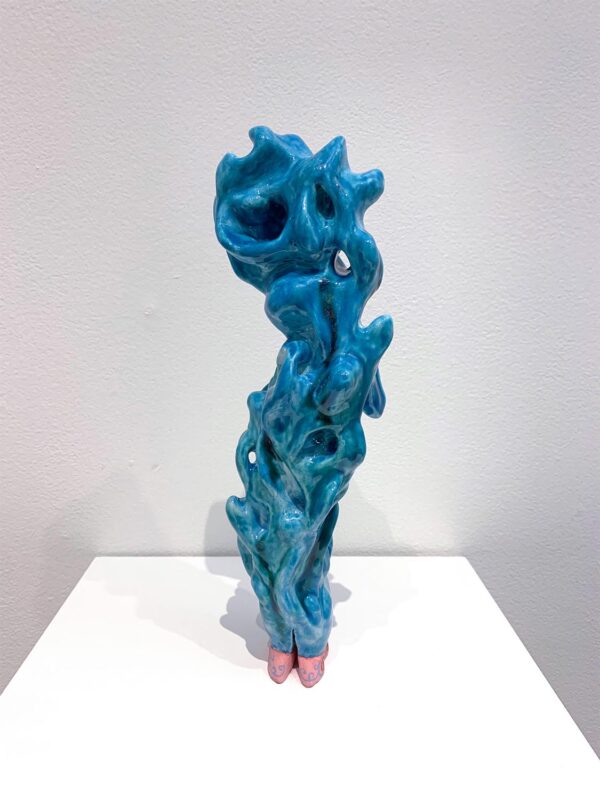 A sculpture made of long wave-like form. The sculpture is painted in blue. At the bottom are two rectangular pieces that look like shoes. The are painted in pink with red details.
