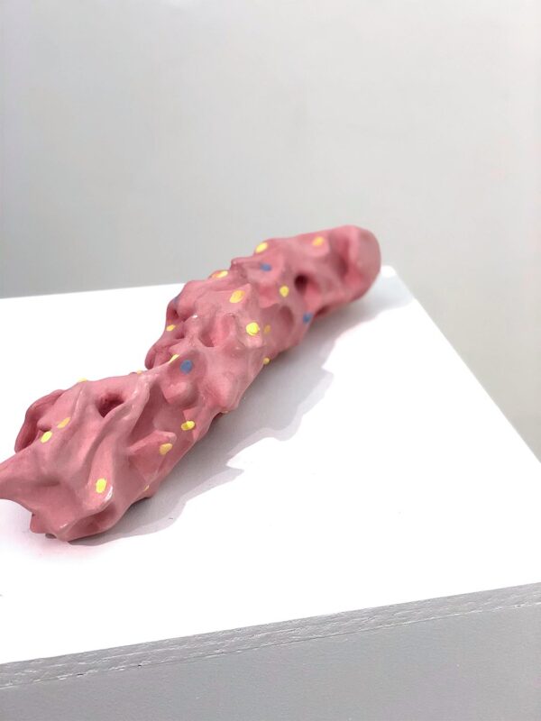 A sculpture made up of long flow-like shapes. The sculpture is  painted pink with colorful dots of yellow and blue.