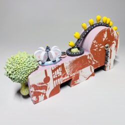 Abstract ceramic sculpture, brightly colored, with a green spiky blob, a pink and red base, and yellow dots along the ridge.