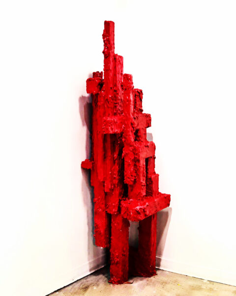 An abstract red sculpture in front of a white background.