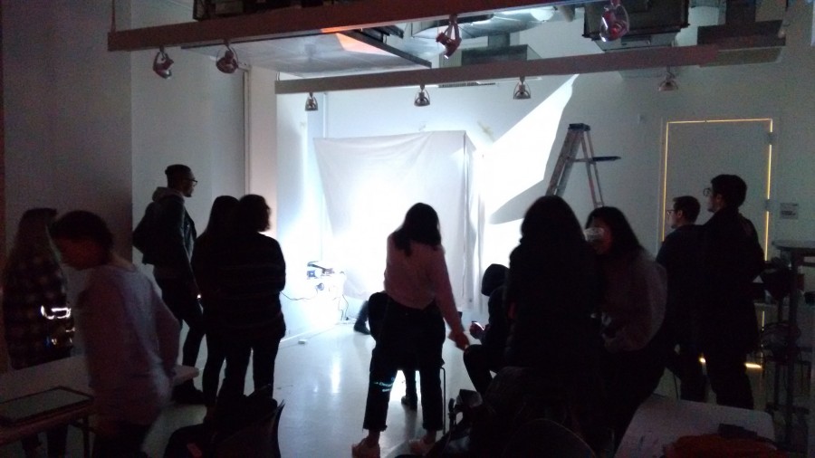 A bunch of people is taking part in the installation of an image projector, looking at a white fabric well illuminated with white light