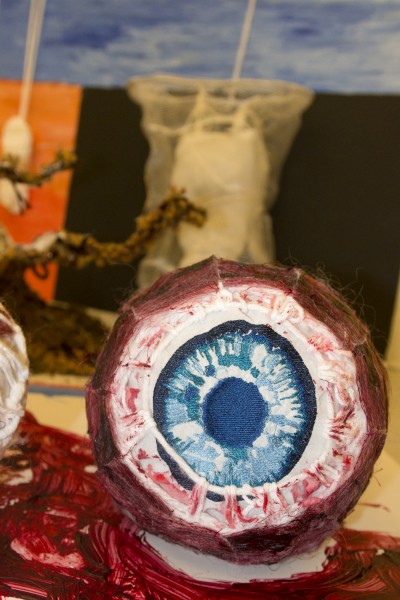 An organic shaped sculpture of a blue eye with different organic shaped objects in the background