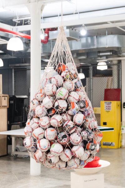 A net suspended from the ceiling holding a bunch of baseballs. Each ball is made up of printed material that has different faces, text, or screenshots printed on them.