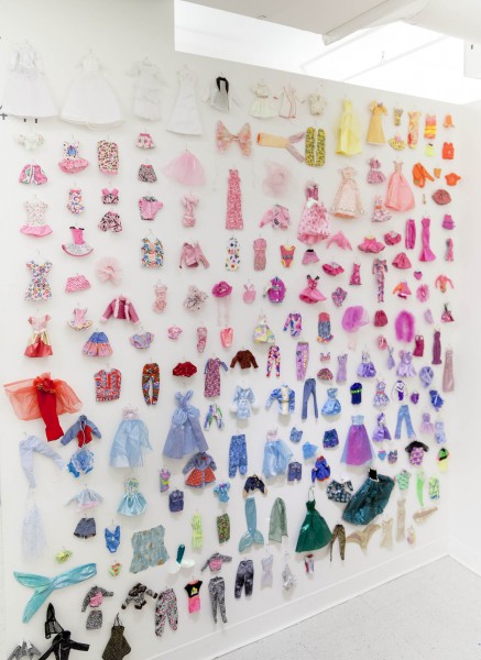 A wall is full of Barbie clothes arranged by their color, from white and light yellow, light pink to red, light blue, violet, and dark green.