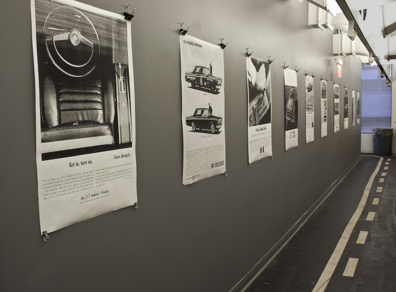 Exhibition view of black and white car posters mounted on a dark grey wall.