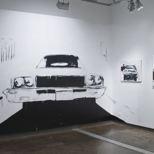 A large-scale car painting on the wall illuminated from the ceiling, and two other car paintings hung on the right wall, all painted in black and white.