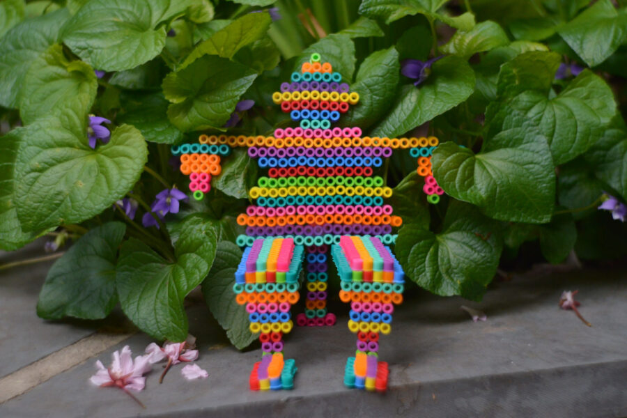 Man made of melty beads sitting next to plant on grounds.