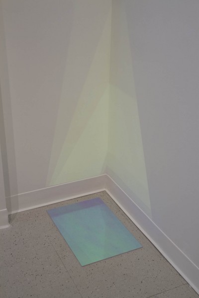 A view of a fluorescent acrylic sheet placed on the ground and reflecting colors on a corner of the wall