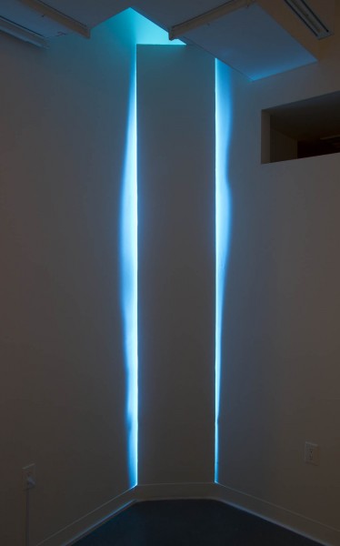 A view of a corner made o a wood structure, and behind the wood structure, blue light is glowing on the left and right side of the wooden structure.