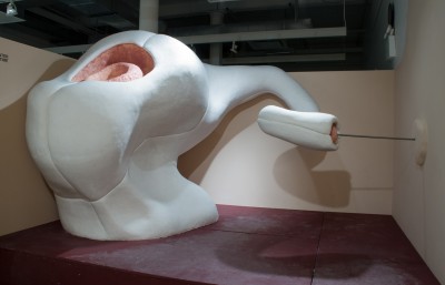 A large scale sculpture with rounded shapes and a longe trumpet side, made of organic material with white outside and orange color on the inside portion visible from the top of the sculpture