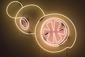 A view of a neon light with rounded shapes and a figure of a citric fruit in the largest round shape.