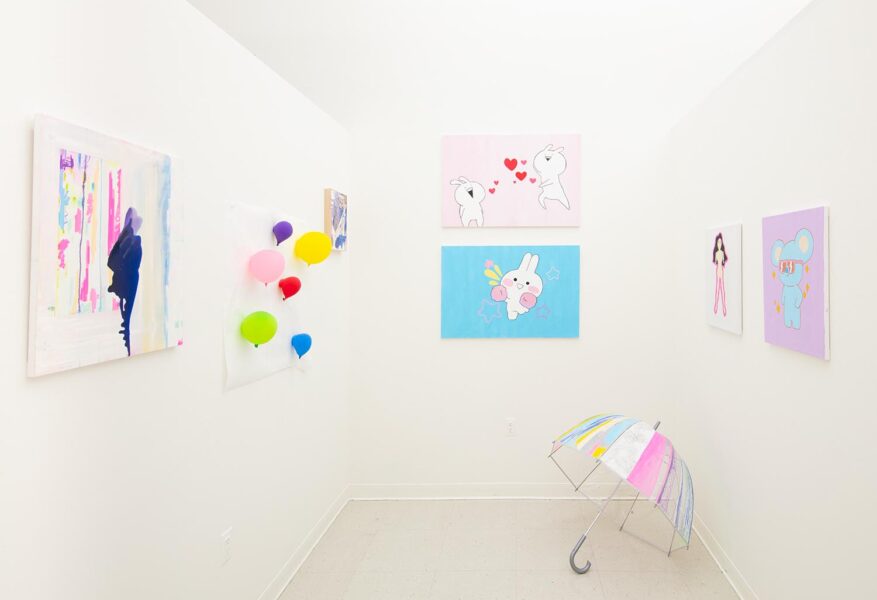 Installation shot of a room with many pink and blue paintings and an umbrella on the floor.