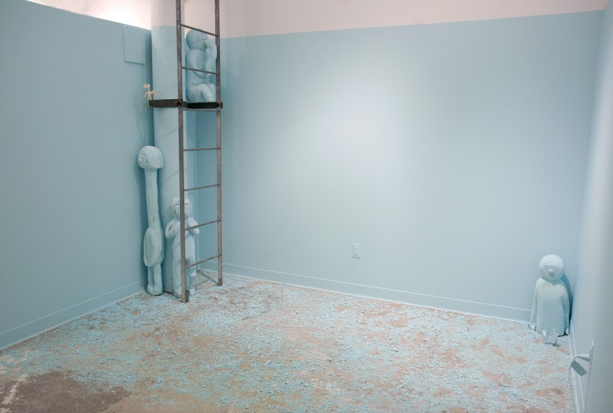Installation view of a ladder, almost all the room painted in baby blue, a petite person sculpture on the near top of the ladder, one small person sculpture placed in the right corner, a tall and a small person sculpture placed near the base of the ladder. All sculptures are painted in baby blue, same as the walls of the wall