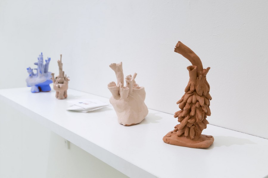 Installation view of four ceramic sculptures with organic curved and rounded shapes, placed on a white shelf