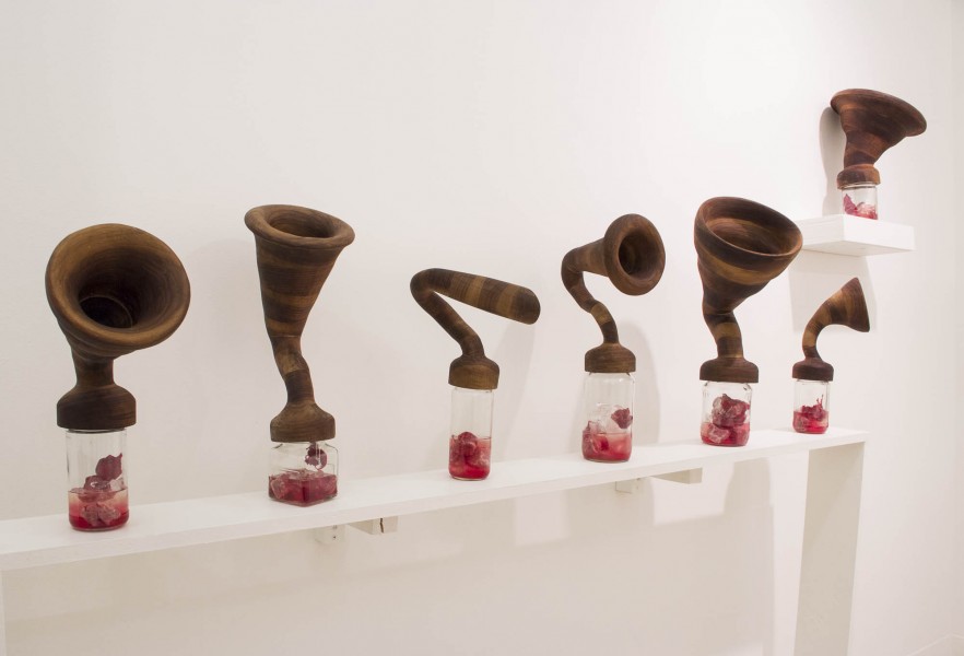 There are six objects made of ceramic of brown color sitting on a shelf.