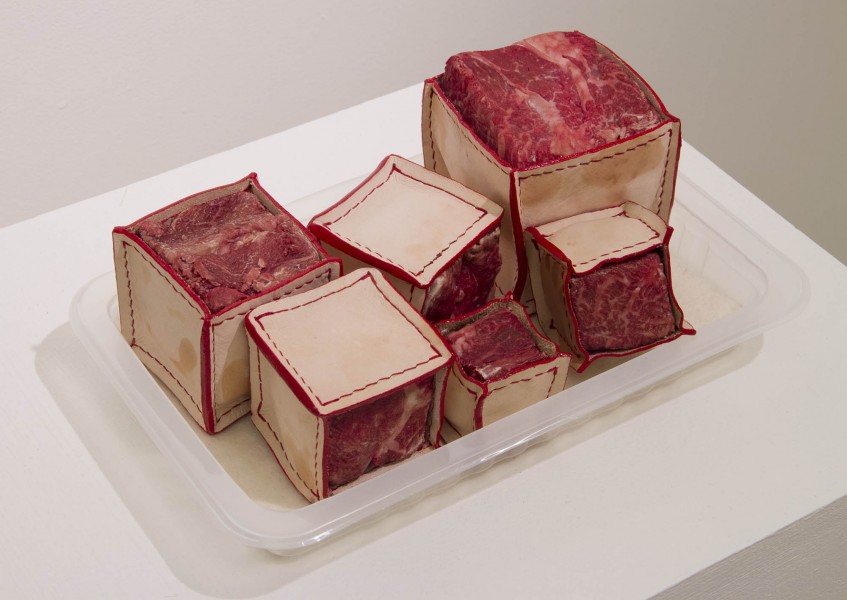A view of multiple small boxes with the top piece of the box made of red meat. Boxes are arranged on a plastic tray.