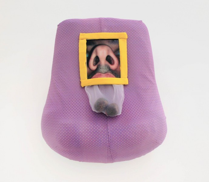 A small photograph of a person's nose with a yellow frame. The picture is placed on a lavender-colored fabric. The picture had a plastic bag with two-sphere brown shapes below it.