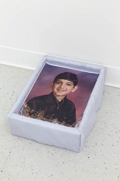 A portrait of a young boy with a black coat and black hair on a blue to violet color background printed on a piece of fabric. The print is placed on a box, and the box is placed on the ground.