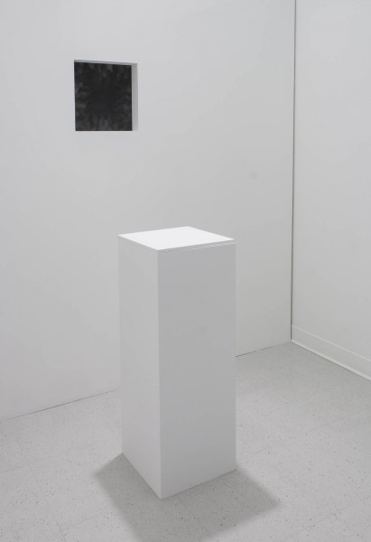 A view of a small black ink-jet print on the wall with a pedestal in front of the wall.