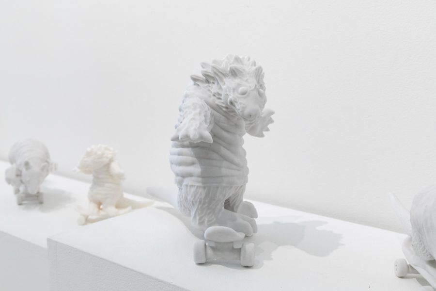 Sculpture by Julio Cesar Candelario. Multiple  white sculptures of animals wearing clothes riding a skateboards.