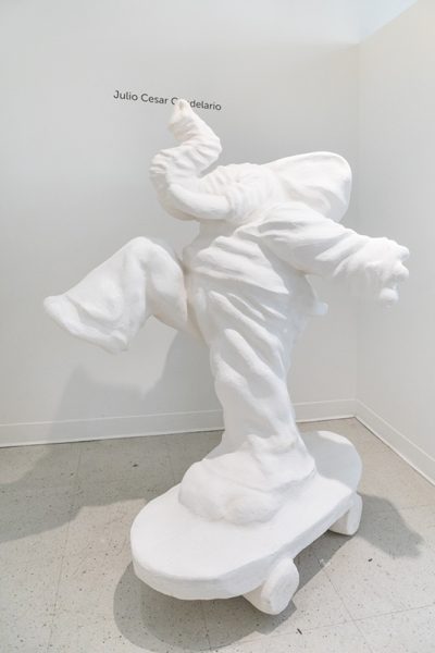 Sculpture by Julio Cesar Candelario. Large white elephant wearing pants and a hoody riding a skateboard.