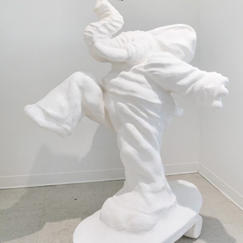 Sculpture by Julio Cesar Candelario. Large white elephant wearing pants and a hoody riding a skateboard.
