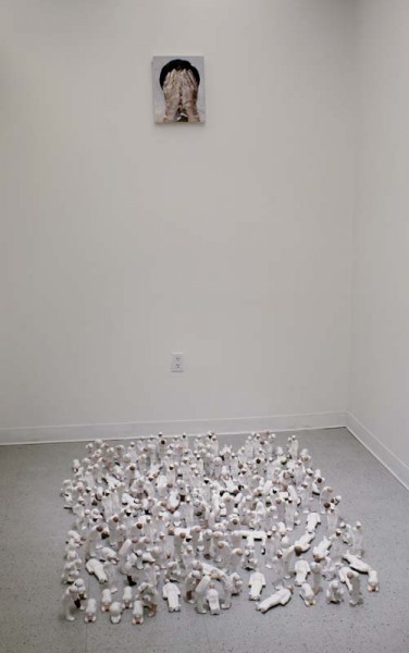 Installation view of small white human figurines on the floor and a portrait painting on the wall of a person covering their face with both hands
