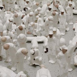 Close-up view of many small human figurines dressed in white with white hats, all bowing.