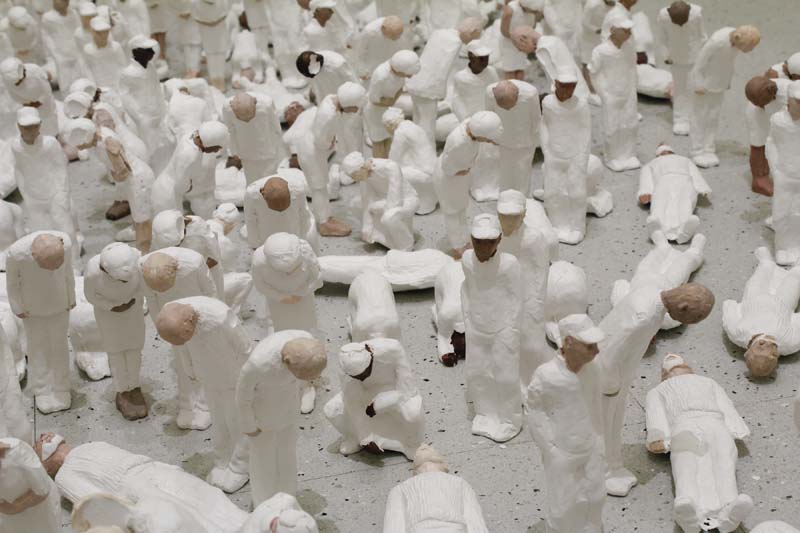  Close-up view of many small human figurines dressed in white with white hats, all bowing.
